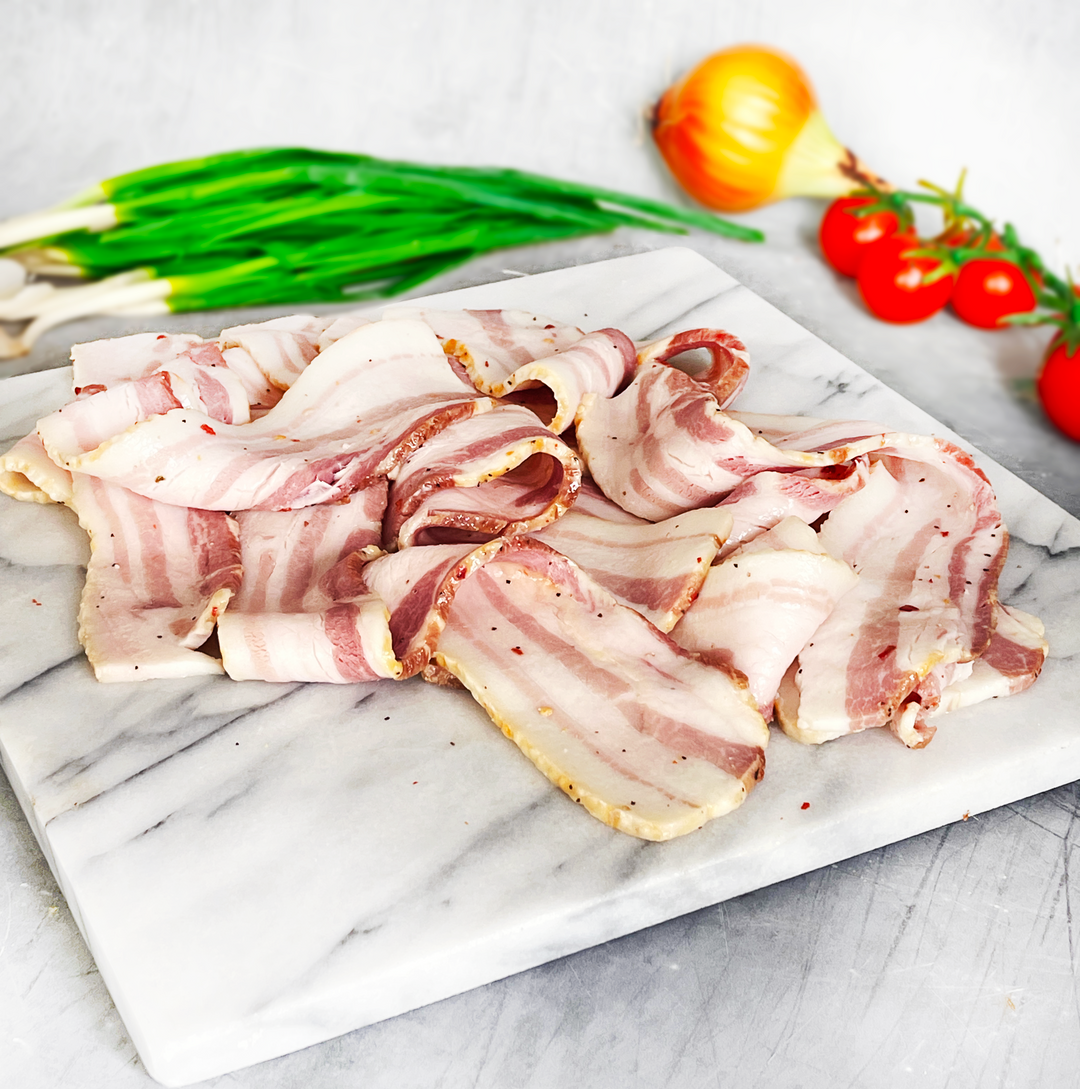 Raw bacon slices on a marble cutting board with vegetables in the background